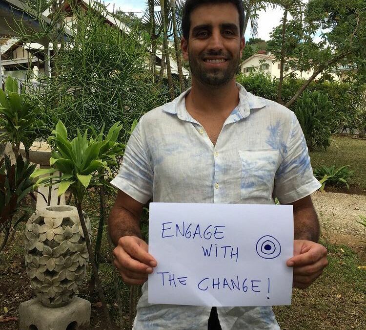 EWB field professional Daniel in Vanuatu holding a sign that says 'Engage with change'