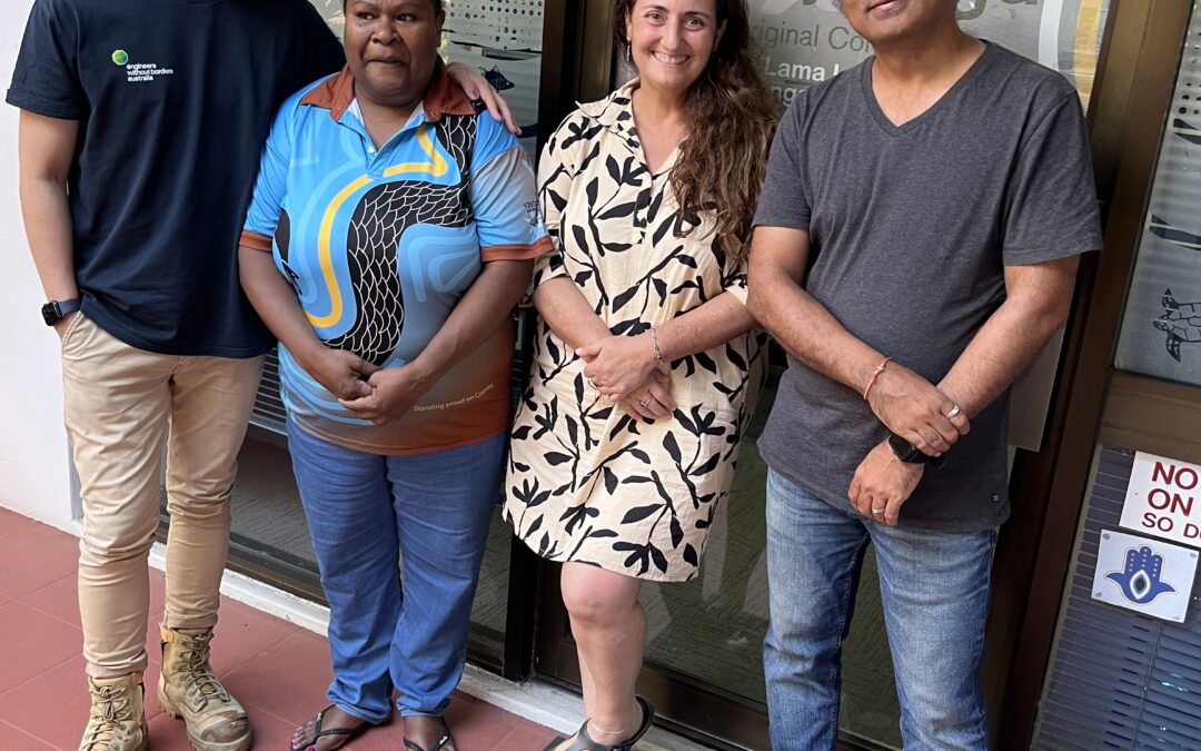 Four adults stand together outside a building entrance with a glass door displaying a partially visible logo and sign.